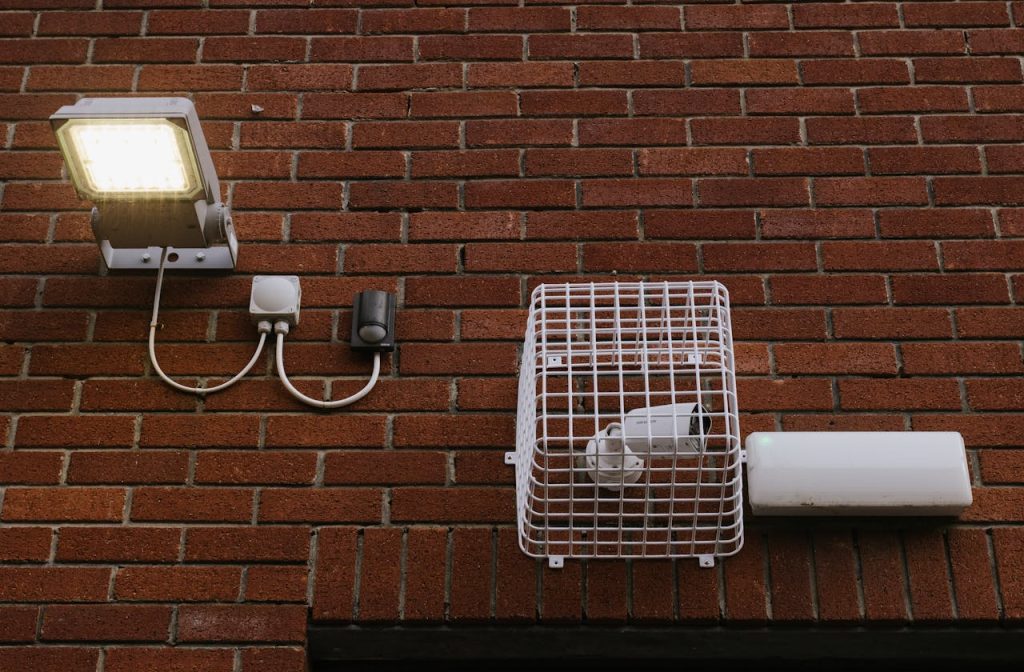 Close-up view of a brick wall featuring a LED light and a caged security camera.