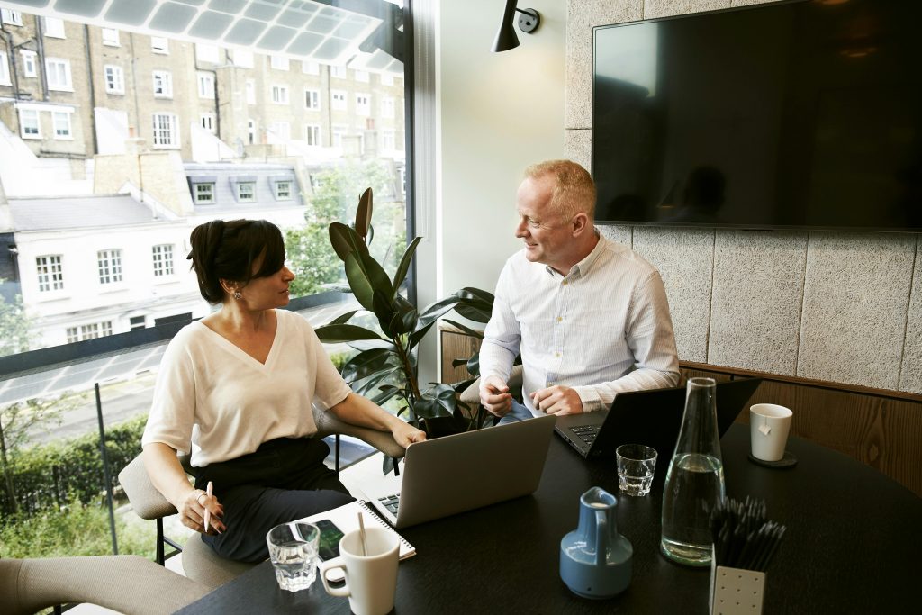 Two business professionals engaging in a team meeting in a modern London office with a large window view.