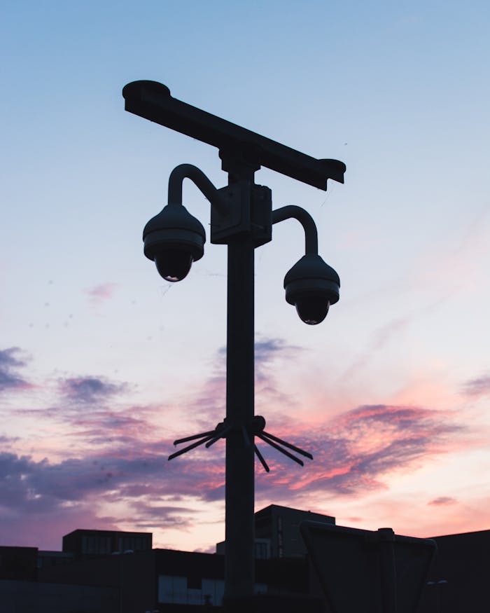 Silhouette of security cameras against a vibrant sunset sky, showcasing modern surveillance technology.